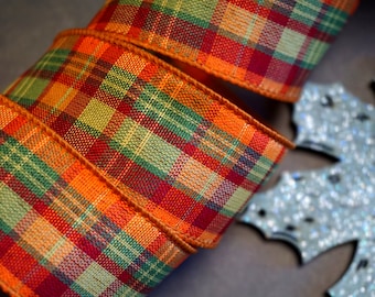 Puede incluir: Cinta a cuadros en tonos naranja, rojo y verde. La cinta tiene una textura tejida y un borde marrón. Probablemente se utiliza para manualidades, envolver regalos o decoraciones de temporada.