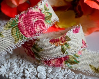 May include: A close-up of a beige fabric ribbon with a pink and green floral pattern. The ribbon has a frayed edge and is folded in half.
