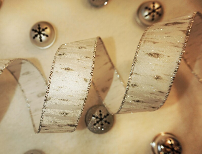 Puede incluir: Cinta blanca con un patr&oacute;n de brillo plateado y un borde plateado. La cinta est&aacute; enroscada y retorcida, creando un dise&ntilde;o decorativo.