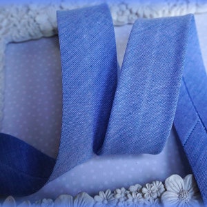 Pode incluir: Um close-up de uma fita de algodão azul com uma superfície texturizada. A fita está dobrada ao meio e as bordas são costuradas juntas.