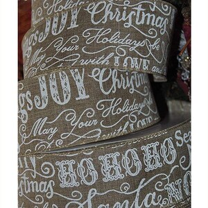 May include: A close-up of three rolls of brown burlap ribbon with white Christmas-themed lettering. The lettering includes "Christmas", "Joy", "Ho Ho Ho", and "Santa".