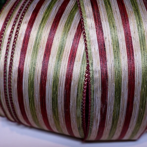 Puede incluir: Primer plano de una cinta decorativa con rayas verticales rojas, verdes y doradas. La cinta tiene un aspecto texturizado y probablemente se utiliza para festividades o envolver regalos. Los bordes están acabados con una costura decorativa.