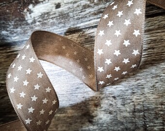 May include: A brown ribbon with white stars printed on it. The ribbon is curled and draped on a rustic wooden surface.