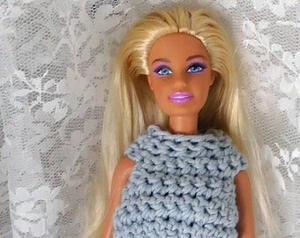 May include: A doll wearing a light blue crocheted dress with a white crocheted belt and blue shoes.