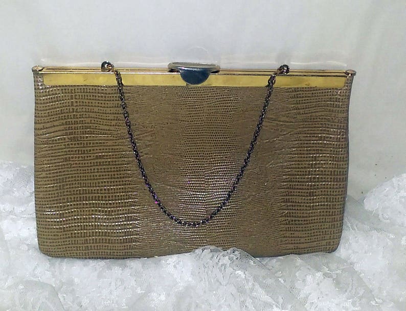 May include: A brown faux leather clutch purse with a gold metal frame and a chain strap. The purse has a textured, embossed pattern.