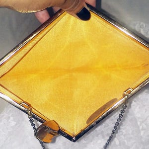 May include: A gold-colored metal clutch purse with a yellow satin lining and a chain strap.