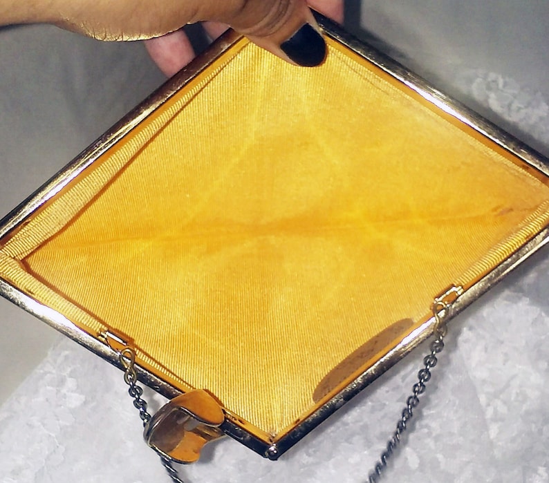 May include: A gold-colored metal clutch purse with a yellow satin lining and a chain strap.
