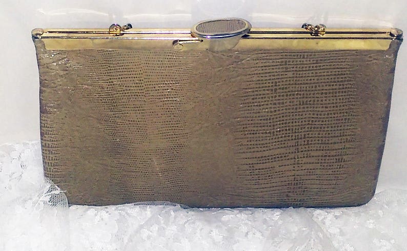May include: A gold-toned clutch purse with a textured, snakeskin-like pattern. The purse has a gold metal clasp and a gold chain strap.