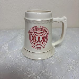 May include: White ceramic beer stein with a red and gold design. The design features the text "88th Annual Convention Hudson Valley Volunteer Firemen's Association Saugerties New York June 16-17-18-1977".
