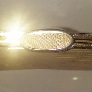 May include: A beige clutch purse with a gold metal frame and a silver oval clasp. The purse has a textured surface.