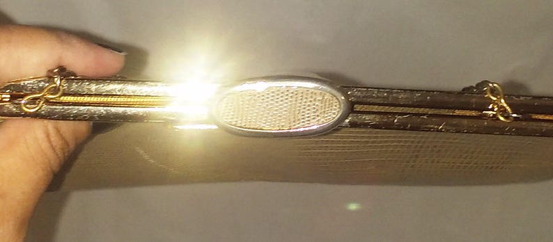 May include: A beige clutch purse with a gold metal frame and a silver oval clasp. The purse has a textured surface.