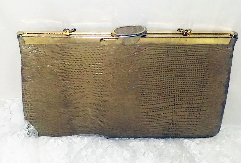 May include: A gold-toned clutch purse with a textured, snakeskin-like pattern. The purse has a metal clasp and a decorative metal piece on the front.