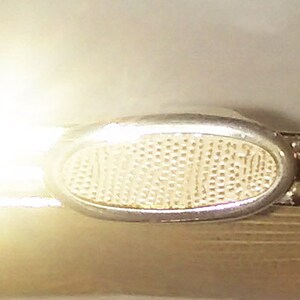 May include: A gold metal clutch purse with a mesh design and a silver clasp. The clasp has a decorative oval shape with a mesh pattern.