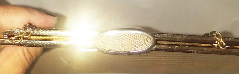 May include: A gold metal clutch purse with a mesh design and a silver clasp. The clasp has a decorative oval shape with a mesh pattern.