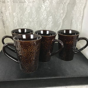 May include: Set of four brown ceramic mugs with a raised floral design. The mugs have a rounded shape and a handle.