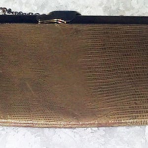 May include: A gold-toned chain purse with a textured, brown leather exterior. The purse has a metal clasp and a chain strap.