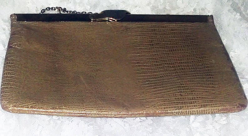 May include: A gold-toned chain purse with a textured, brown leather exterior. The purse has a metal clasp and a chain strap.