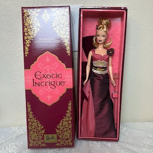 Może przedstawiać: Lalka Barbie w burgundowej i różowej sukni z złotymi akcentami. Lalka znajduje się w pudełku z napisem "Exotic Intrigue" i "Barbie Collector's Edition".