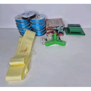 May include: A craft supply set including multiple spools of bright blue ribbon, a long strip of pale yellow ribbon, a Pro Bow Maker box, a green three-pronged plastic tool, and a green rectangular metal bow-making device with silver hardware.