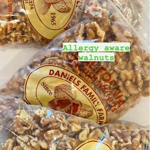 May include: Clear plastic bags filled with shelled walnuts. The bags have a yellow label with the text "DANIELS FAMILY FARM" and "Since 1965". The text "Allergy aware walnuts" is also visible.