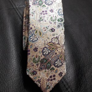 May include: A beige silk tie with a floral pattern in shades of purple, green, and blue.
