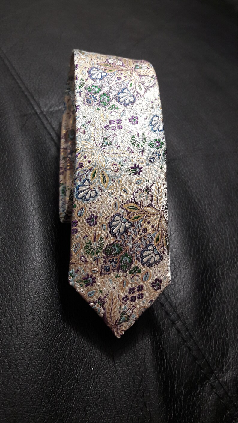 May include: A beige silk tie with a floral pattern in shades of purple, green, and blue.
