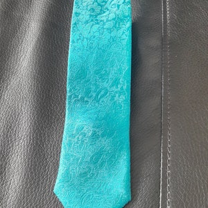May include: A teal blue patterned tie with a paisley design.