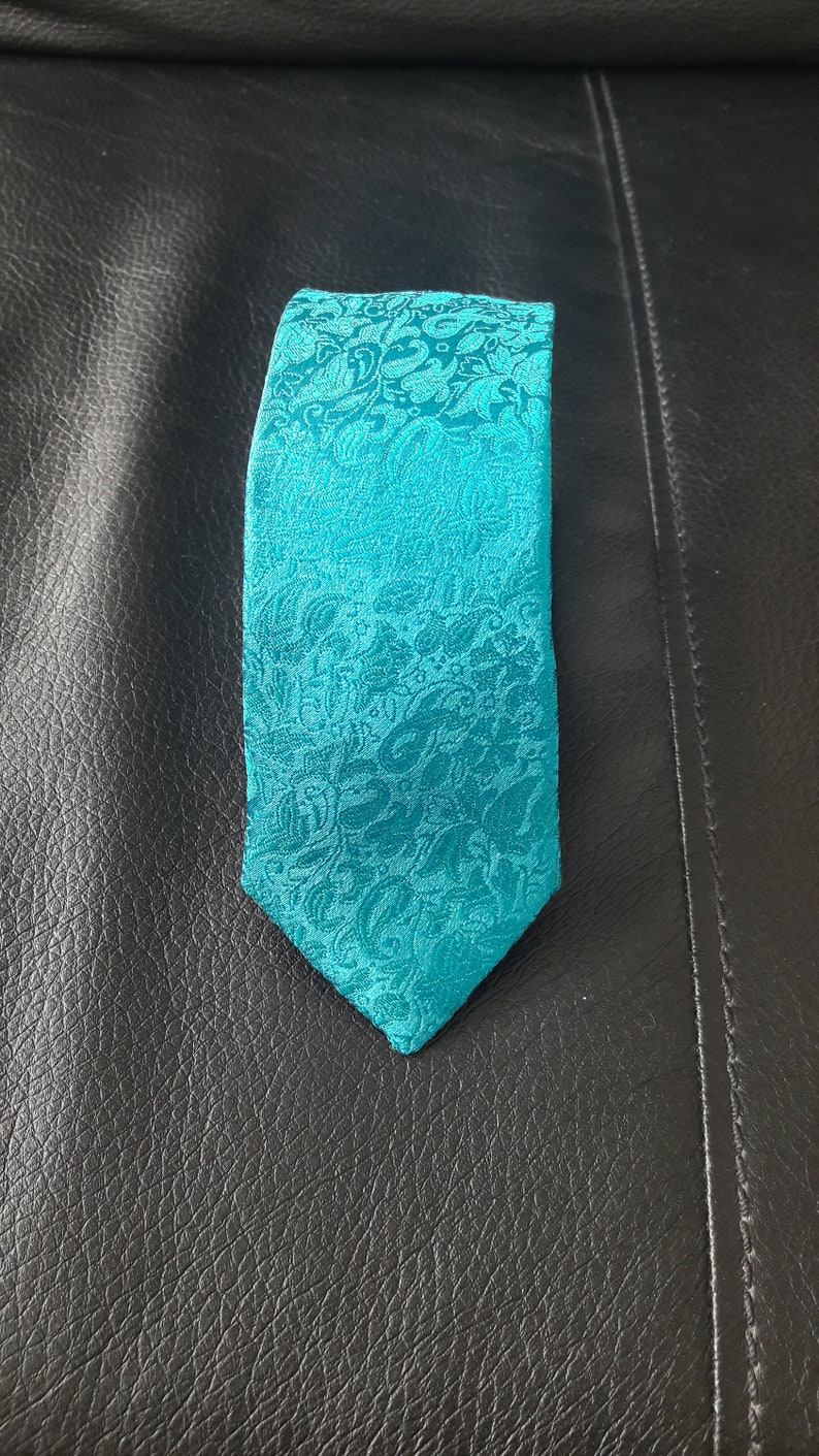 May include: A teal blue patterned tie with a paisley design.