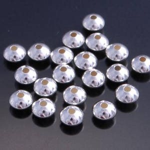 May include: A collection of silver-toned metal beads with a domed shape. The beads have a textured surface and a small hole in the center.