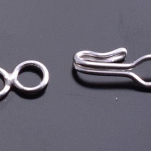 May include: Two silver metal jewelry findings. One is a figure eight shape and the other is a hook with a loop.