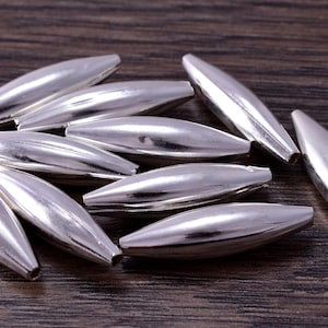 May include: A group of silver-colored metal beads, each shaped like an elongated oval with a smooth, shiny finish.
