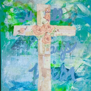 May include: Abstract art piece featuring a cross adorned with peach-colored roses. The cross is made of layered paper with a floral pattern. The background is a mix of blue, green, and white brushstrokes, with the words "I will pray" in light blue.