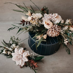 May include: A floral arrangement featuring a dark blue vase filled with a variety of dried flowers and greenery. A smaller matching arrangement is placed to the left. The flowers include beige dahlias, roses, and various green leaves.