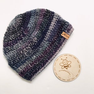 May include: A purple and grey striped crocheted beanie with a brown leather tag that says "@nickybee.crochet".