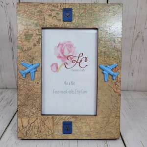May include: A wooden picture frame with a world map design. The frame is decorated with blue airplanes and blue passport stamps. The frame is 4 inches by 6 inches and is available on Etsy at FaustinasCrafts.Etsy.com.