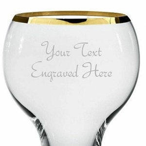 May include: A clear glass goblet with a gold rim. The goblet has a wide bowl and a tall, slender stem. The words "Your Text Engraved Here" are etched into the glass.