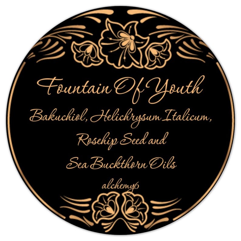 May include: A circular black label with a thin gold border and gold floral accents at the top and bottom. The text reads: Fountain Of Youth, Bakuchiol, Helichrysum Italicum, Rosehip Seed and Sea Buckthorn Oils, and the word alchemy6 in gold script.