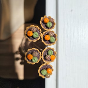 May include: Six miniature flower pots with brown rims and green and orange flowers. The pots are arranged in a vertical line.