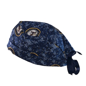 May include: A blue and white patterned surgical scrub cap with a navy blue tie. The cap has a geometric pattern with small white dots and a larger pattern of gold and white circles.
