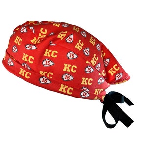 May include: Red and yellow patterned surgical scrub hat with a black tie. The pattern features the letters "KC" and the number "15" repeated throughout.