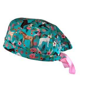 May include: A turquoise blue surgical scrub hat with a pink tie. The hat features a repeating pattern of horses and flowers.