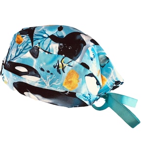 May include: A blue and black patterned surgical scrub hat with a turquoise tie. The pattern features orcas, fish, and coral.