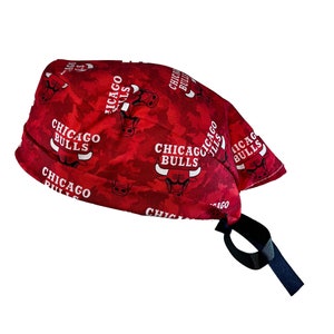 May include: Red and white surgical scrub hat with a repeating pattern of the Chicago Bulls logo. The hat has a black tie.