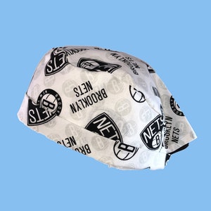 May include: White fabric hat with a black and white Brooklyn Nets logo pattern. The hat is folded and the logo is visible on the front and sides.