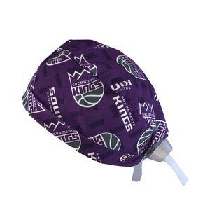 May include: Purple scrub hat with a repeating pattern of the Sacramento Kings logo. The logo features a basketball with a crown above it and the words "Sacramento Kings".