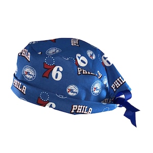 May include: Blue and red patterned surgical scrub hat with a tie. The hat features the Philadelphia 76ers logo and the word "PHILA" repeated throughout.