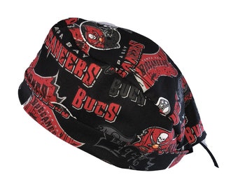 May include: Black and red fabric scrub hat with a repeated pattern of the Tampa Bay Buccaneers logo. The logo features a pirate skull and crossbones with the words "Tampa Bay Buccaneers" and "Bucs" written around it.