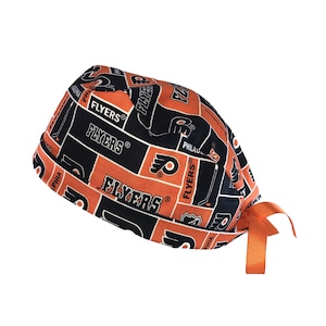 May include: A black and orange surgical scrub hat with the Philadelphia Flyers logo and the words "Flyers" repeated throughout the fabric. The hat has a tie on the side.