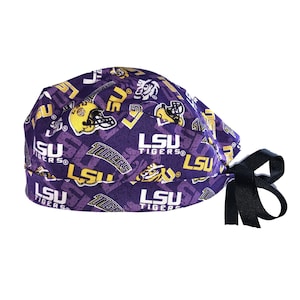 May include: A purple scrub cap featuring a repeating pattern of the LSU Tigers logo, yellow LSU text, and yellow football helmets. The cap has a wide band and black fabric ties at the back to secure the fit, showcasing a collegiate sports theme.