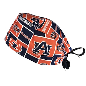 May include: A patterned surgical scrub cap featuring the Auburn University logo and the word "Tigers" in white on a navy blue and orange background. The cap has a tie closure and is designed for medical professionals.